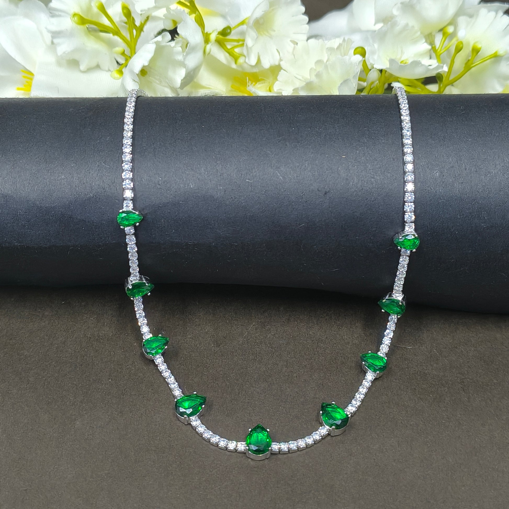 Bracelet with green gemstones on a dark background with white flowers.