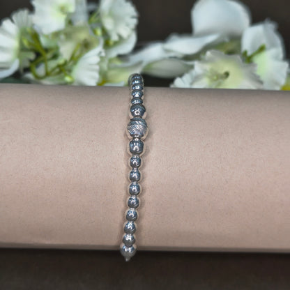 Silver beaded bracelet on a wrist with white flowers in the background