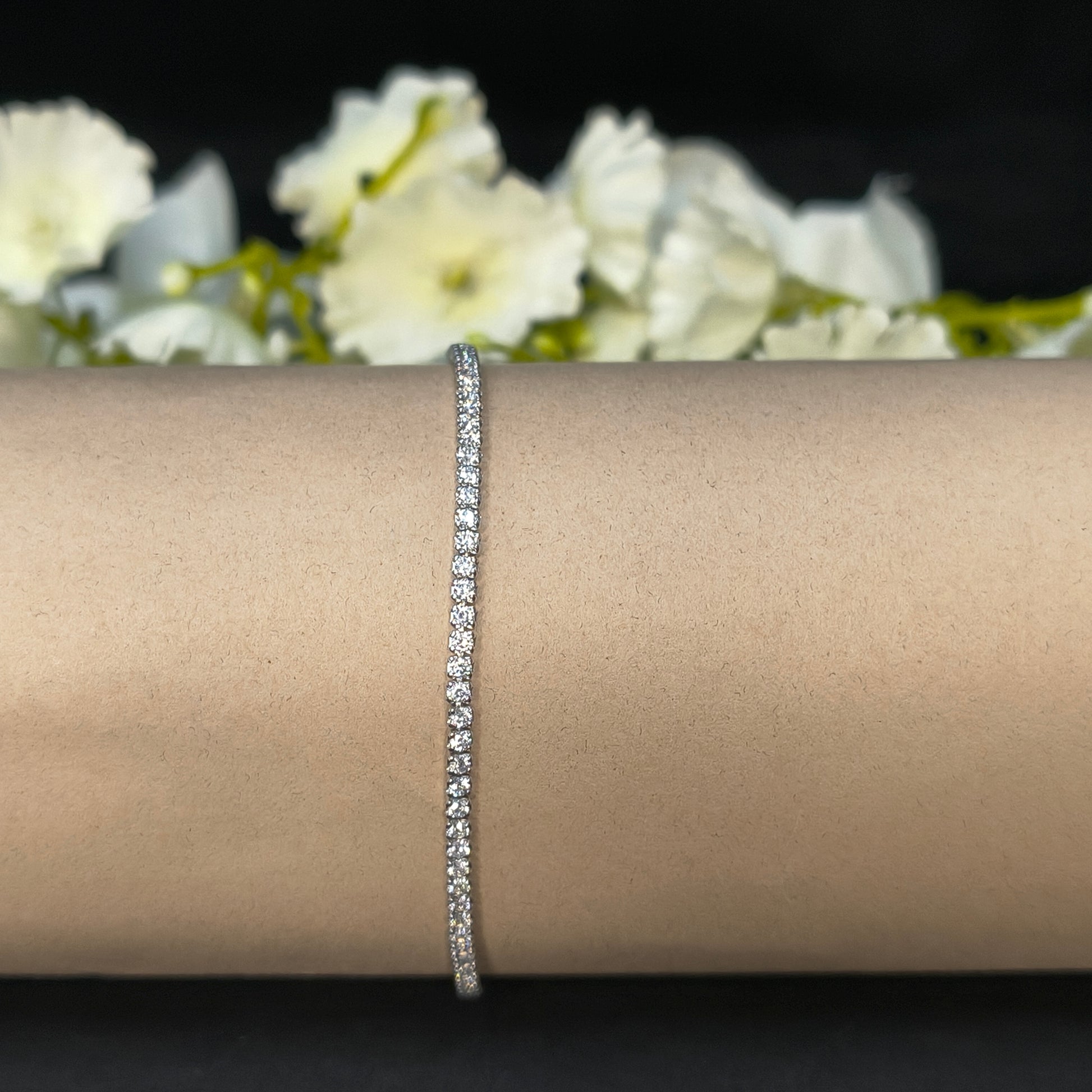 Silver bracelet on a person's wrist with a blurred floral background
