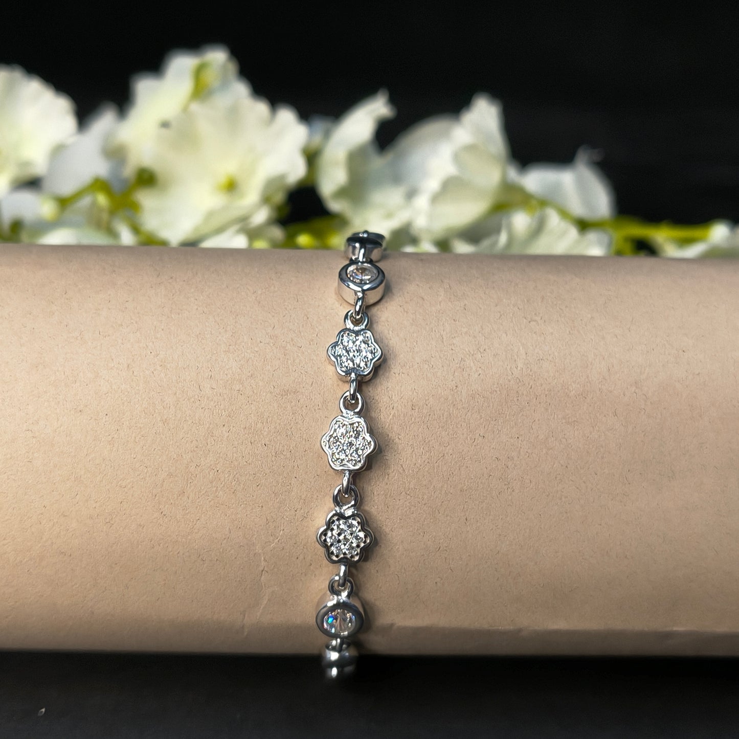 Silver bracelet with floral designs on a wrist against a dark background with white flowers.