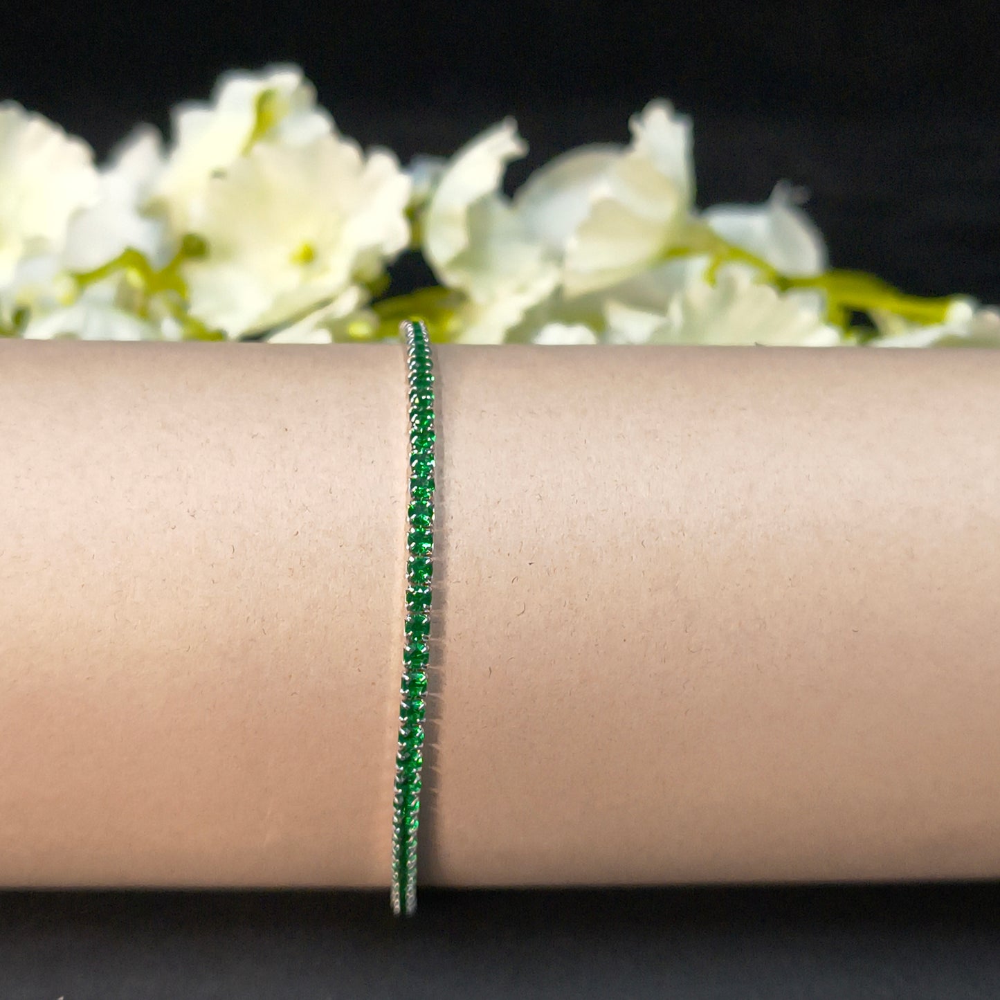 Green bracelet on a wrist with white flowers in the background