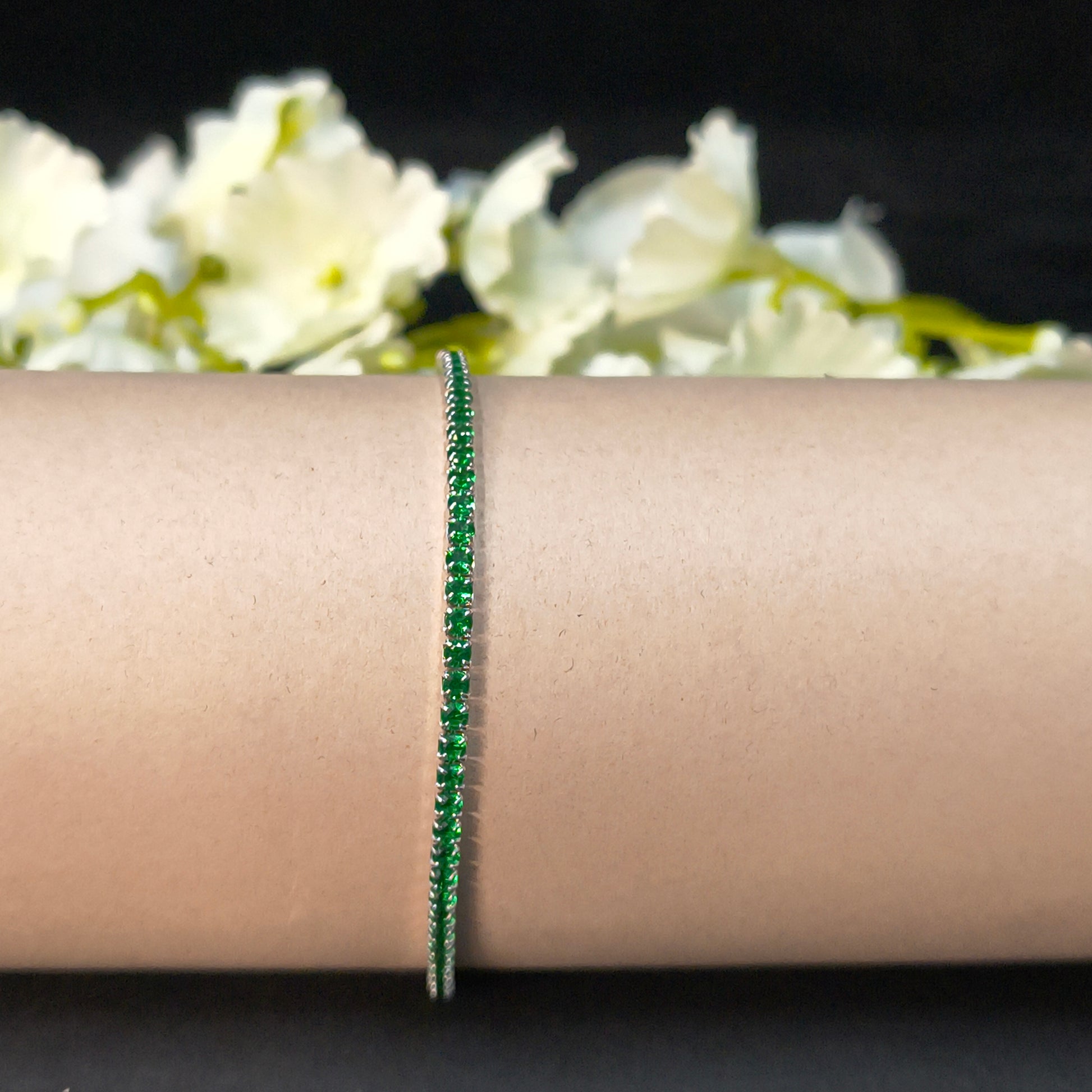 Green bracelet on a wrist with white flowers in the background