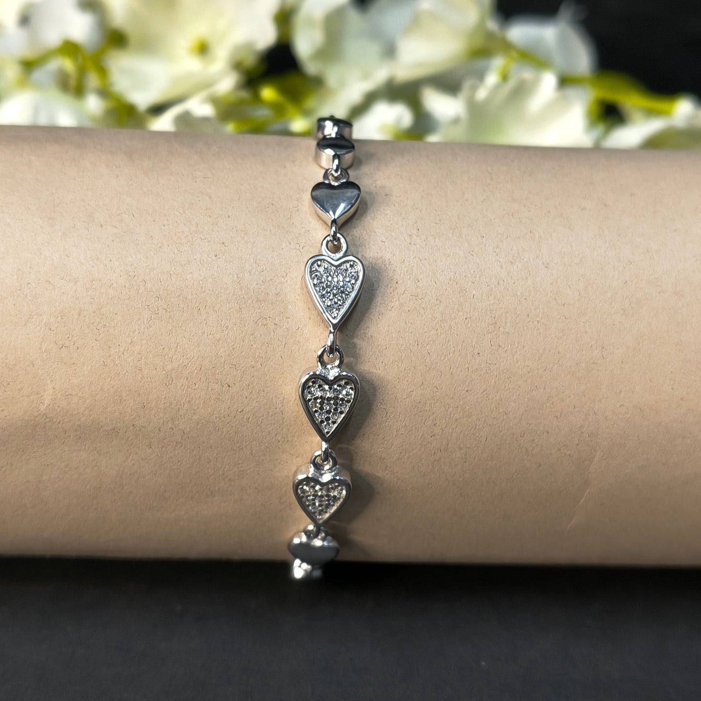 Silver bracelet with heart-shaped charms on a wrist against a neutral background