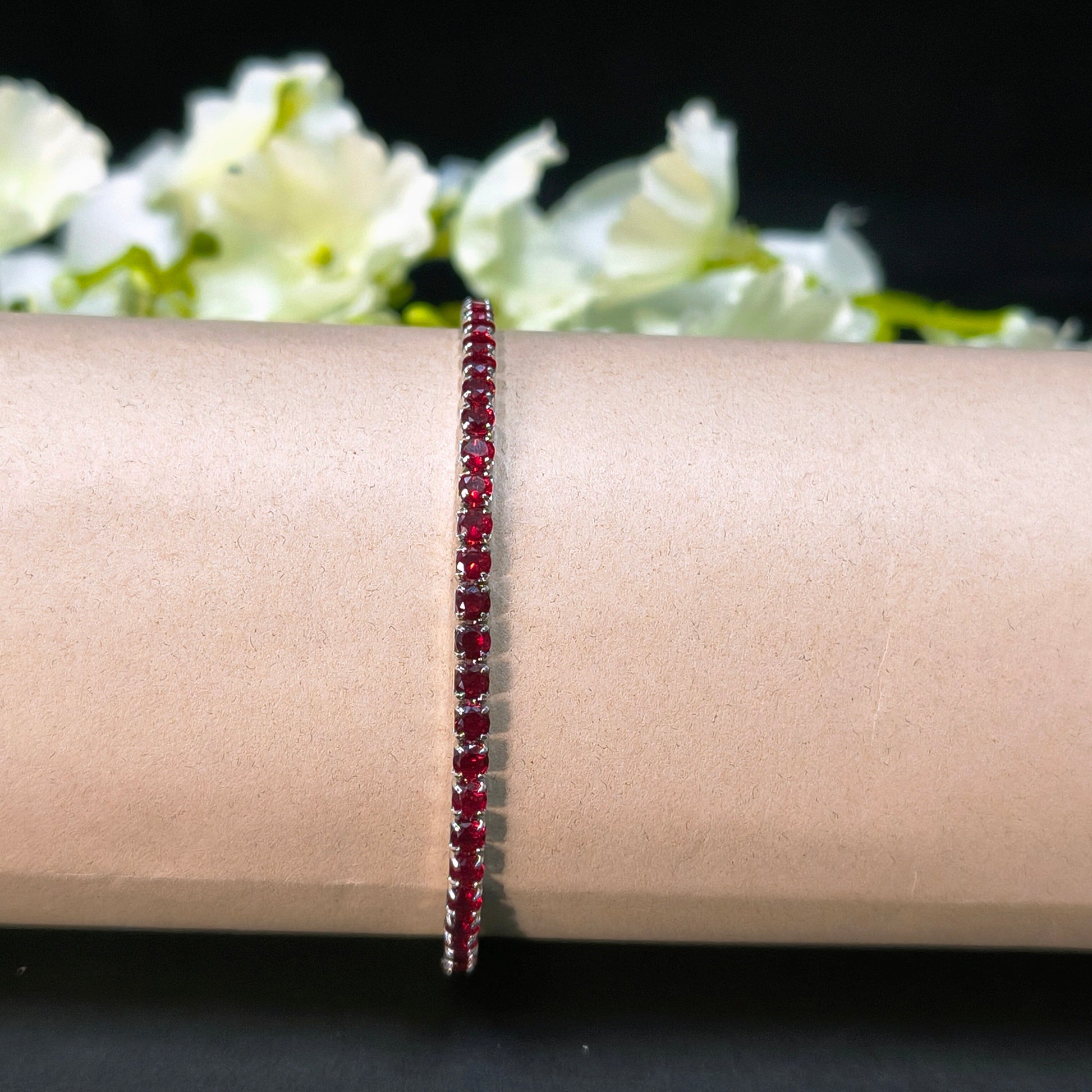 Red beaded bracelet on a wrist with a blurred floral background