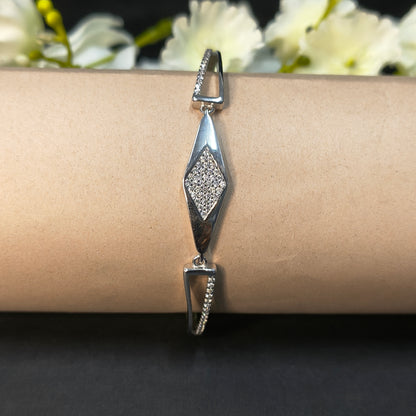 Silver bracelet with diamond-shaped design on a wrist against a dark background with white flowers.