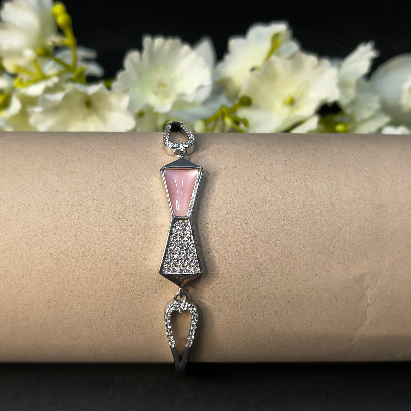 Bracelet with bow design on a cardboard stand with flowers in the background