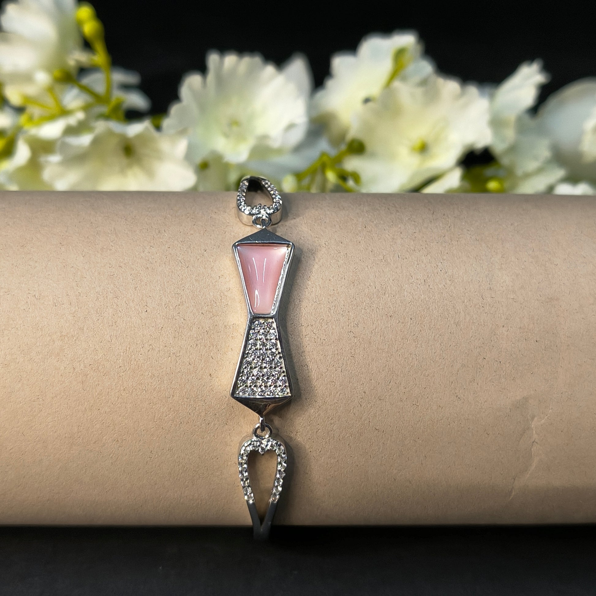 Bracelet with bow design on a cardboard stand with flowers in the background