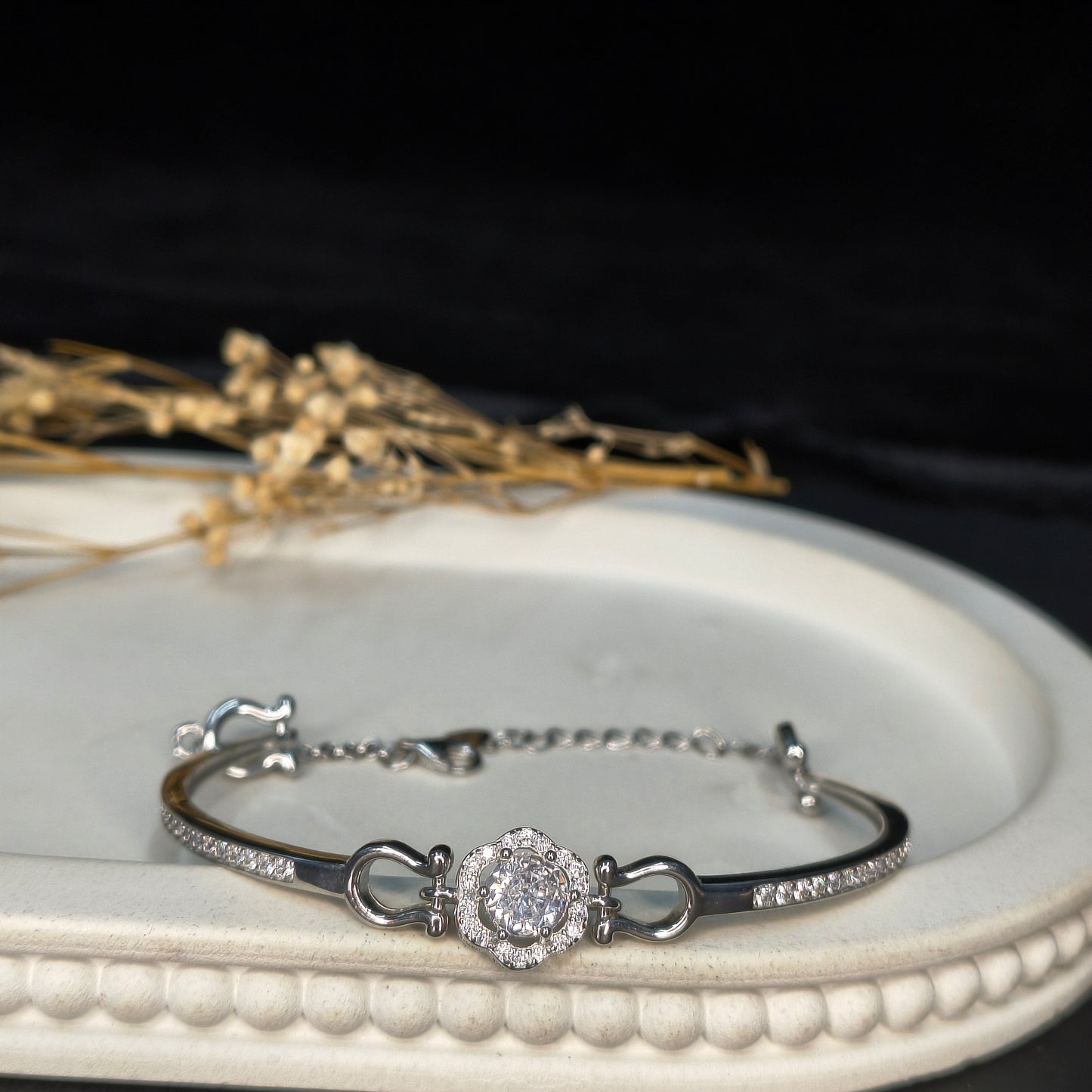 Silver bracelet with a diamond-like stone on a white circular stand with a black background