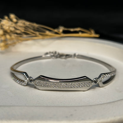 Silver bracelet with diamond accents on a white surface with dried flowers in the background