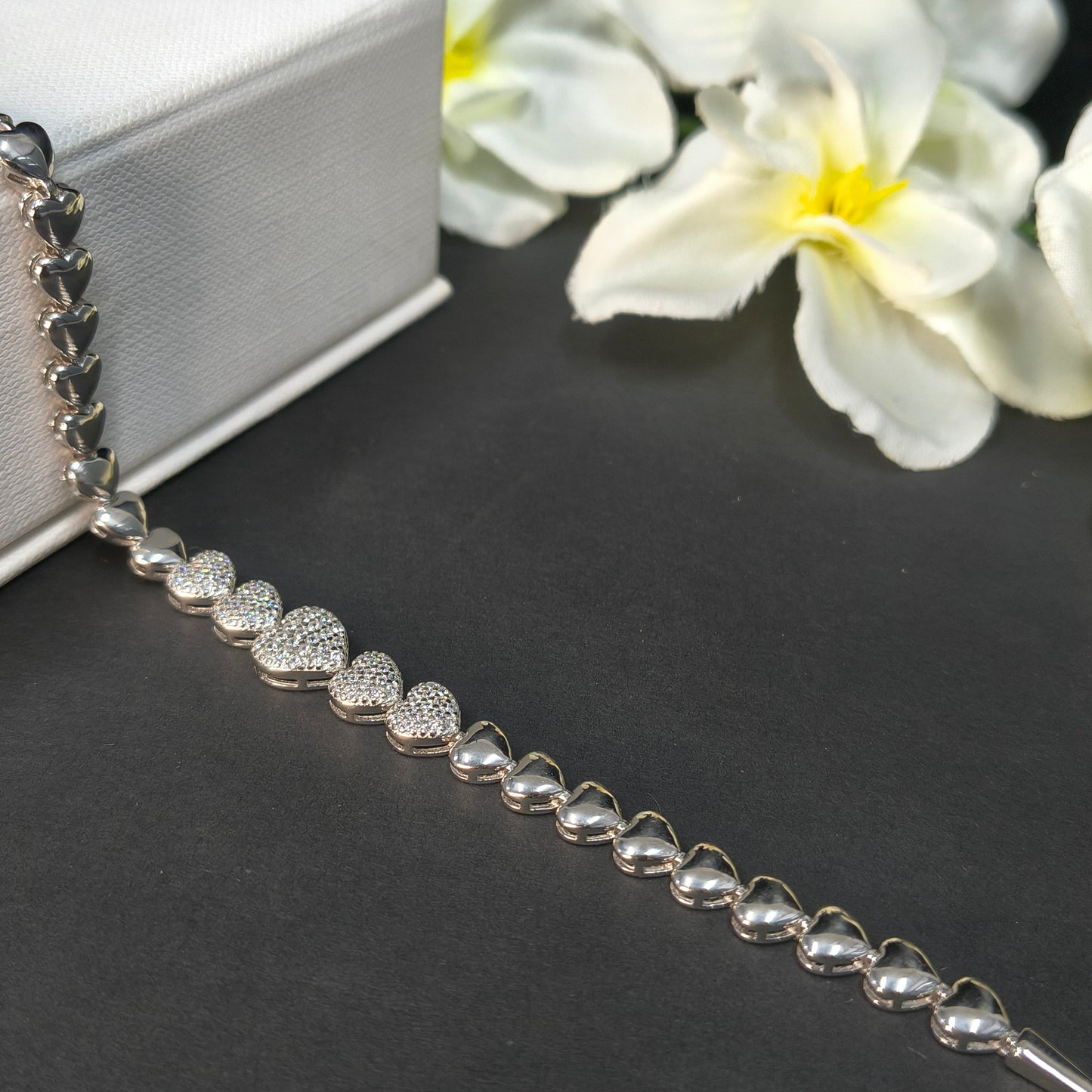 Silver beaded necklace on a dark surface with white flowers in the background