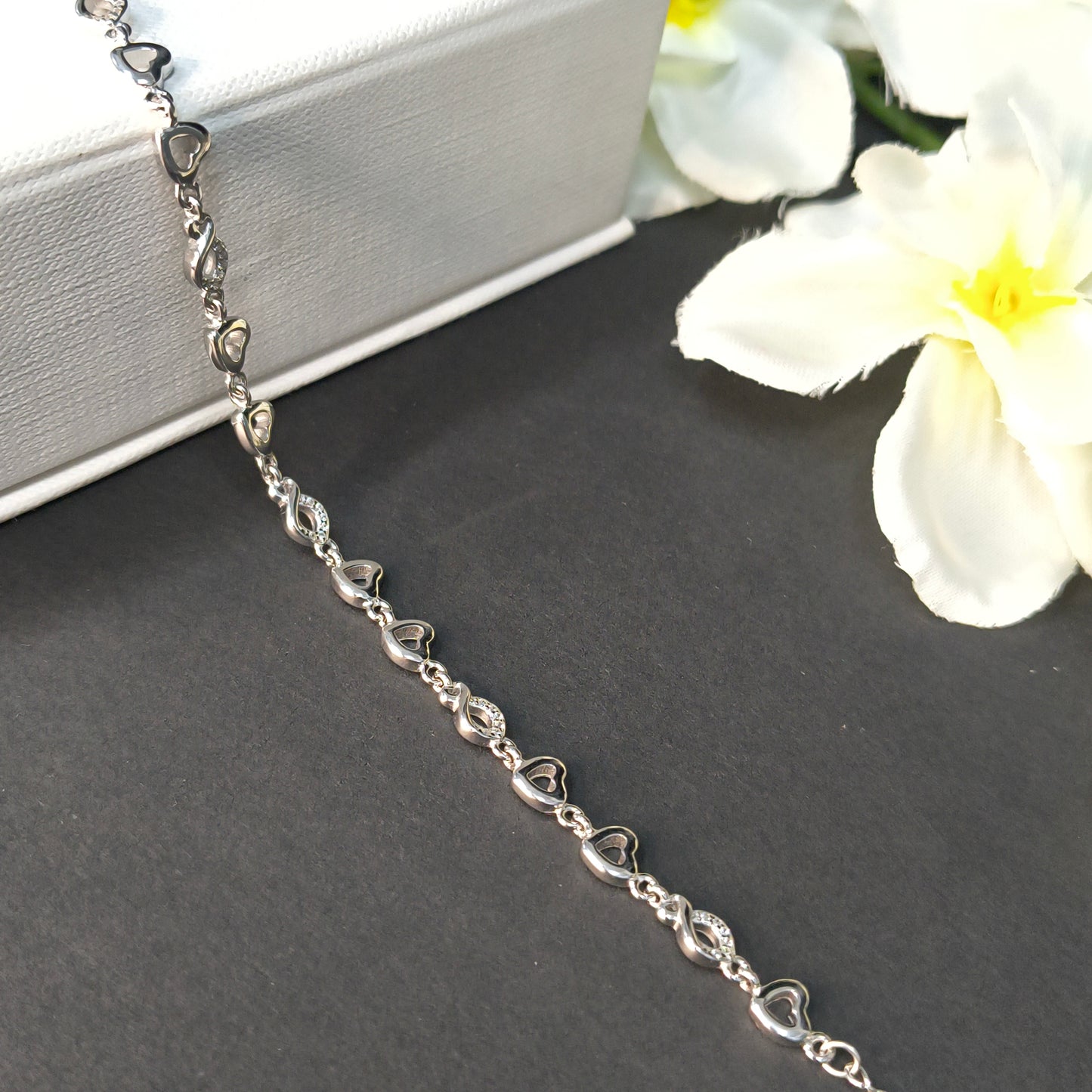 Silver heart-shaped bracelet on a dark surface with white flowers in the background