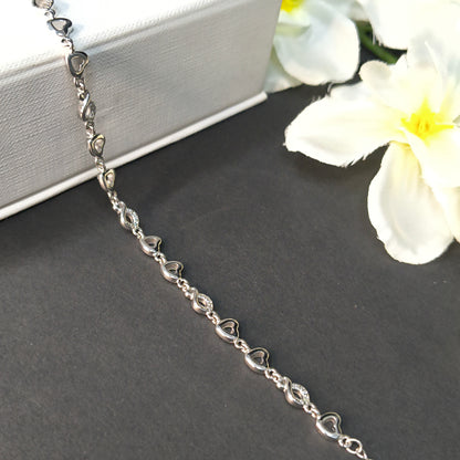 Silver heart-shaped bracelet on a dark surface with white flowers in the background