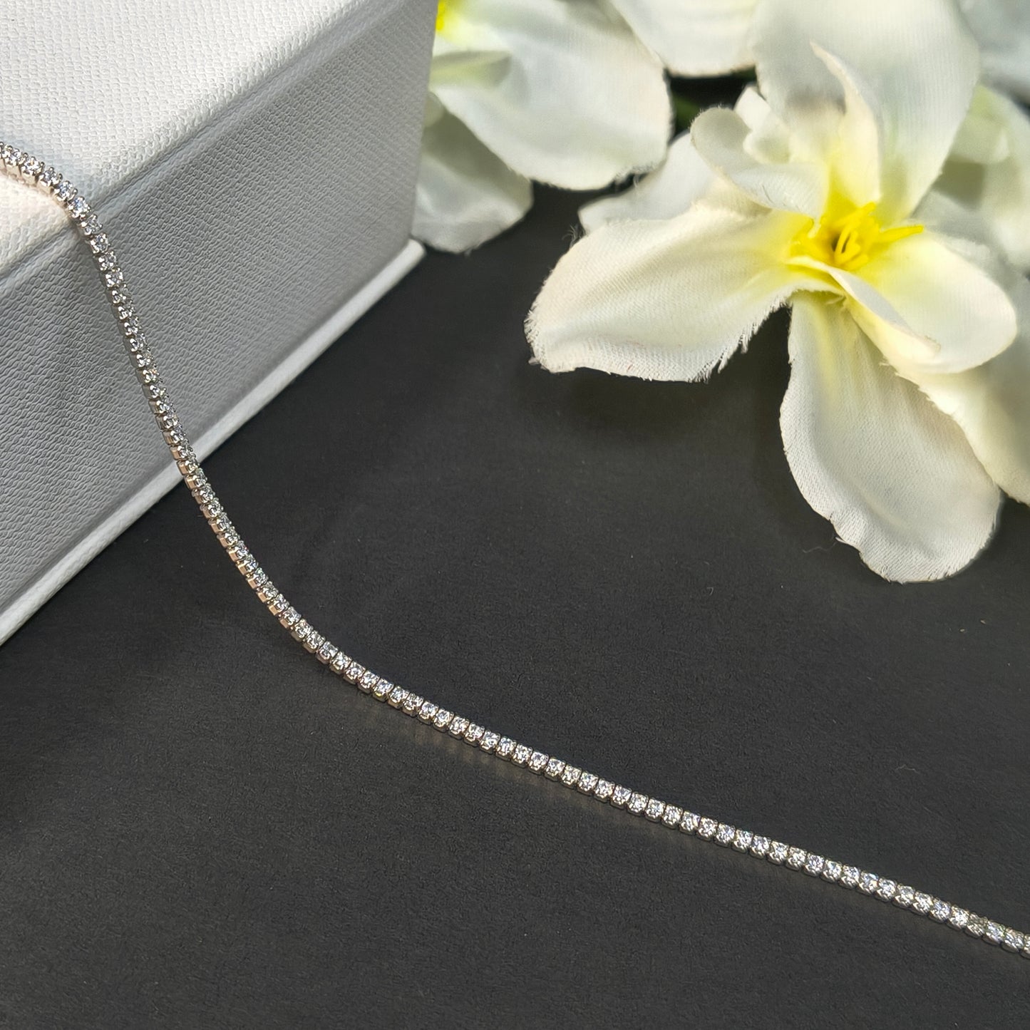 Silver chain necklace on a dark surface with white flowers