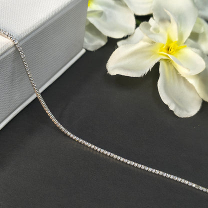 Silver chain necklace on a dark surface with white flowers