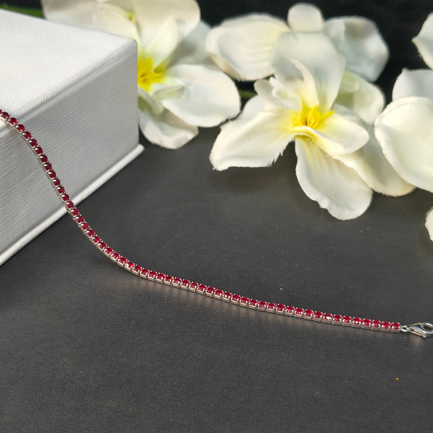 Necklace with red gemstones on a dark background with white flowers