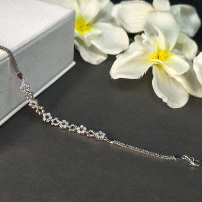 Silver bracelet with floral design on a dark surface with white flowers.