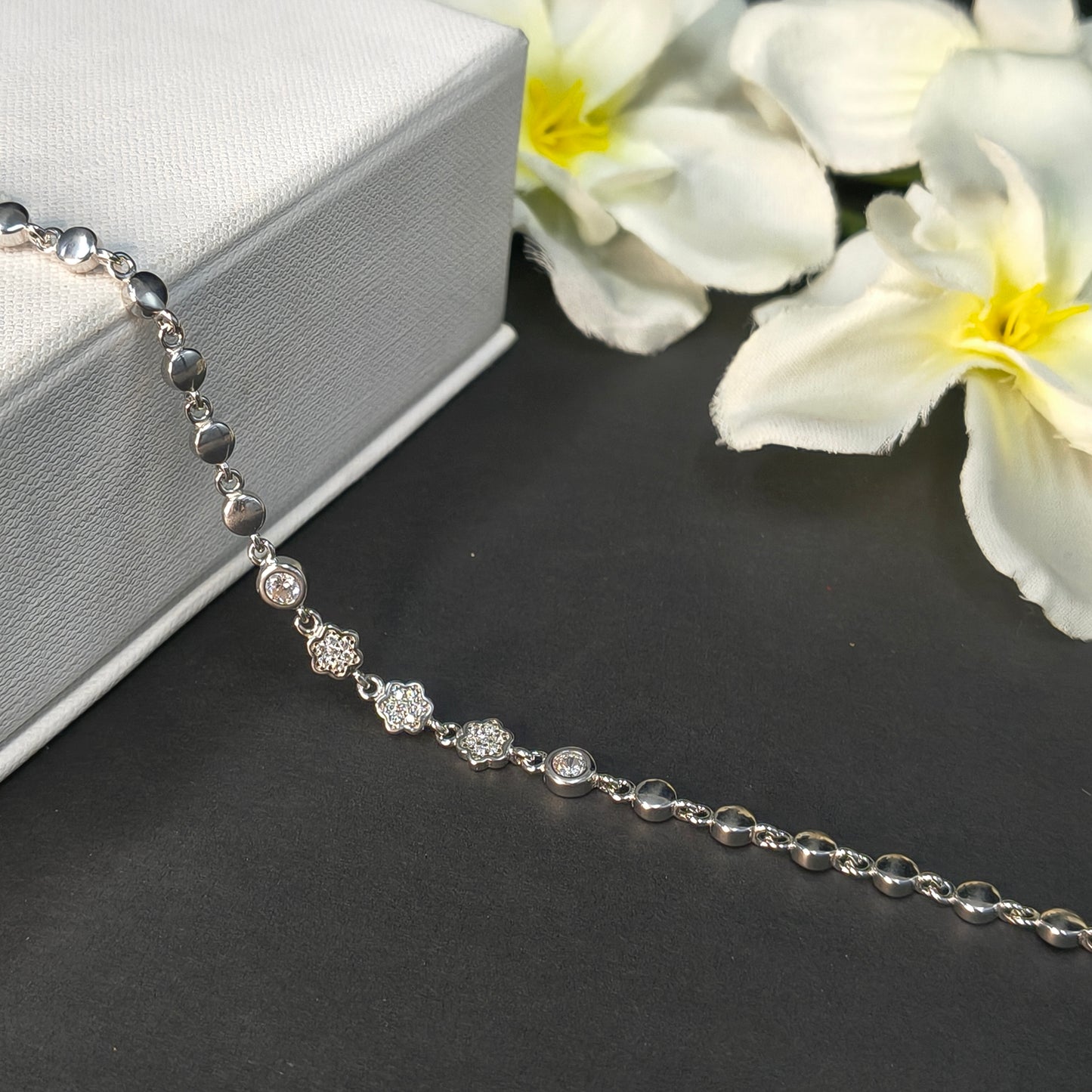 Silver necklace with floral elements on a dark surface with white flowers.