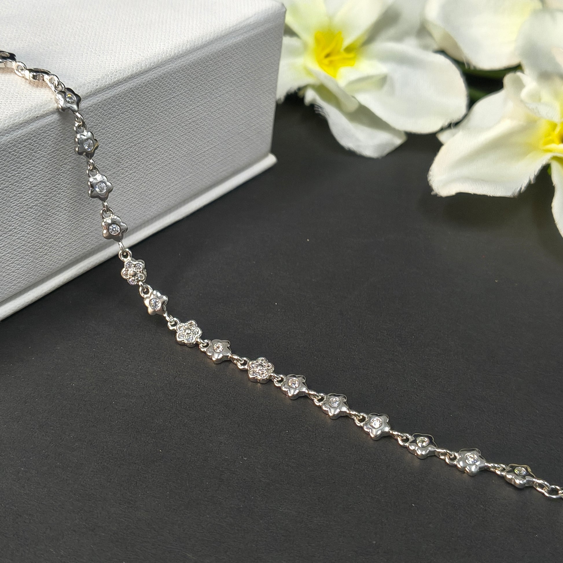 Silver necklace with floral design on a dark surface with flowers in the background