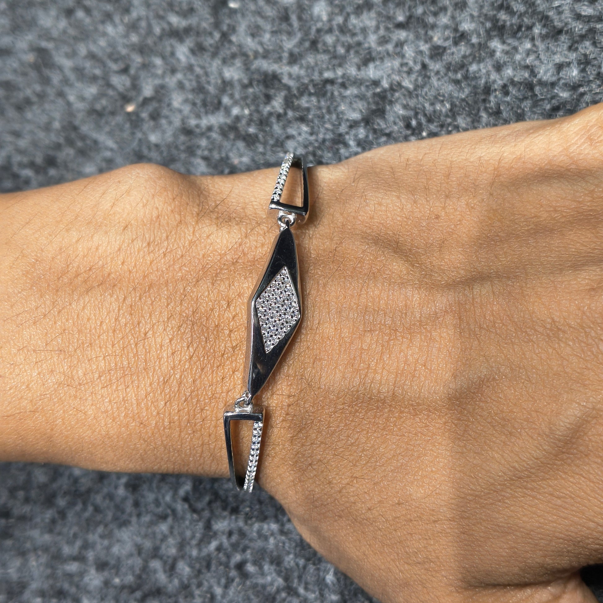 Silver bracelet with geometric design on a wrist against a gray pavement background