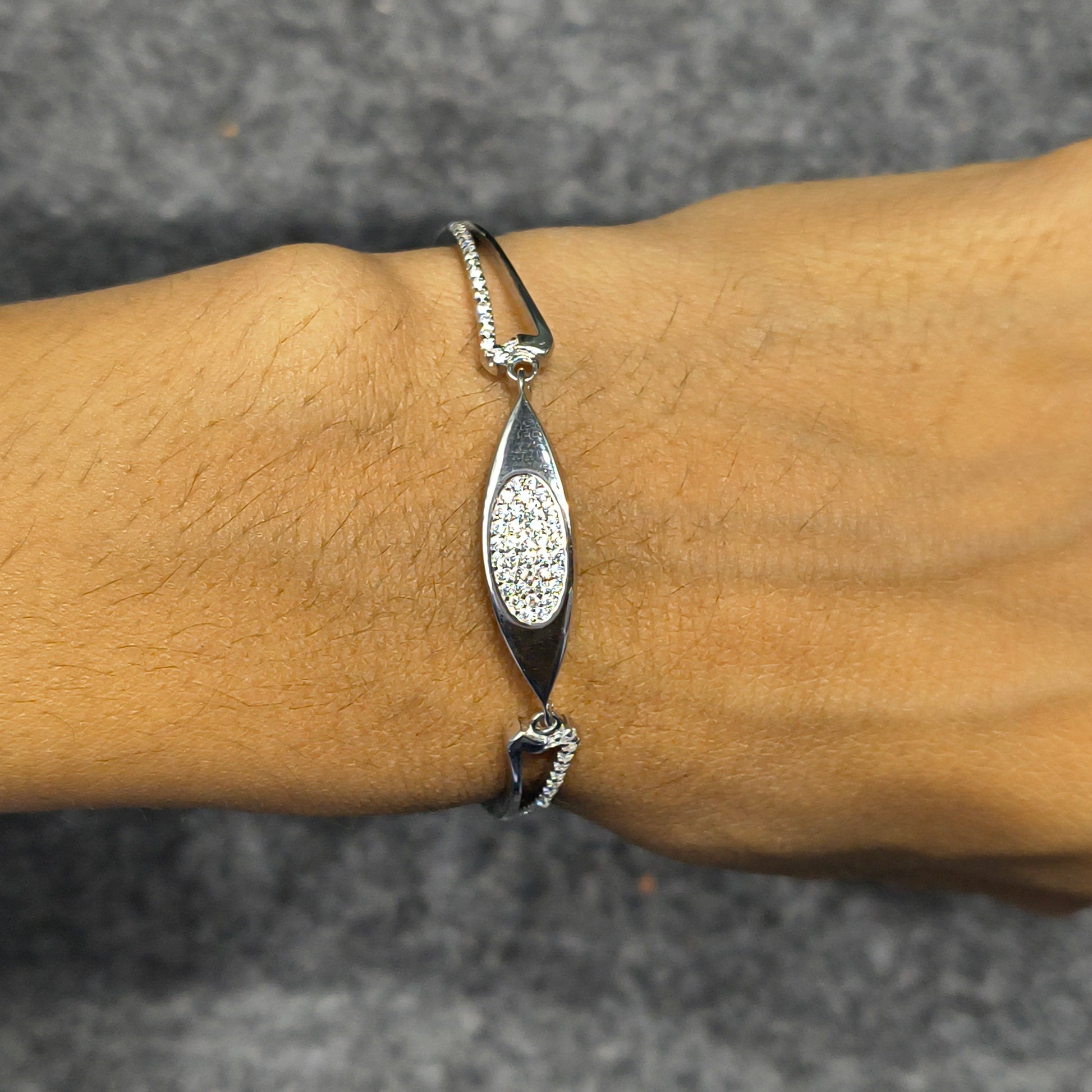 Silver bracelet with a decorative pendant on a wrist against a gray background