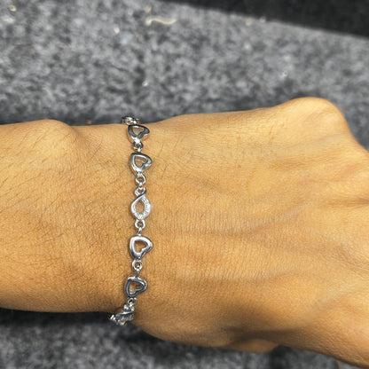 Silver heart-shaped bracelet on a wrist against a gray background