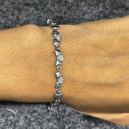 Silver bracelet with heart-shaped charms on a wrist against a gray background