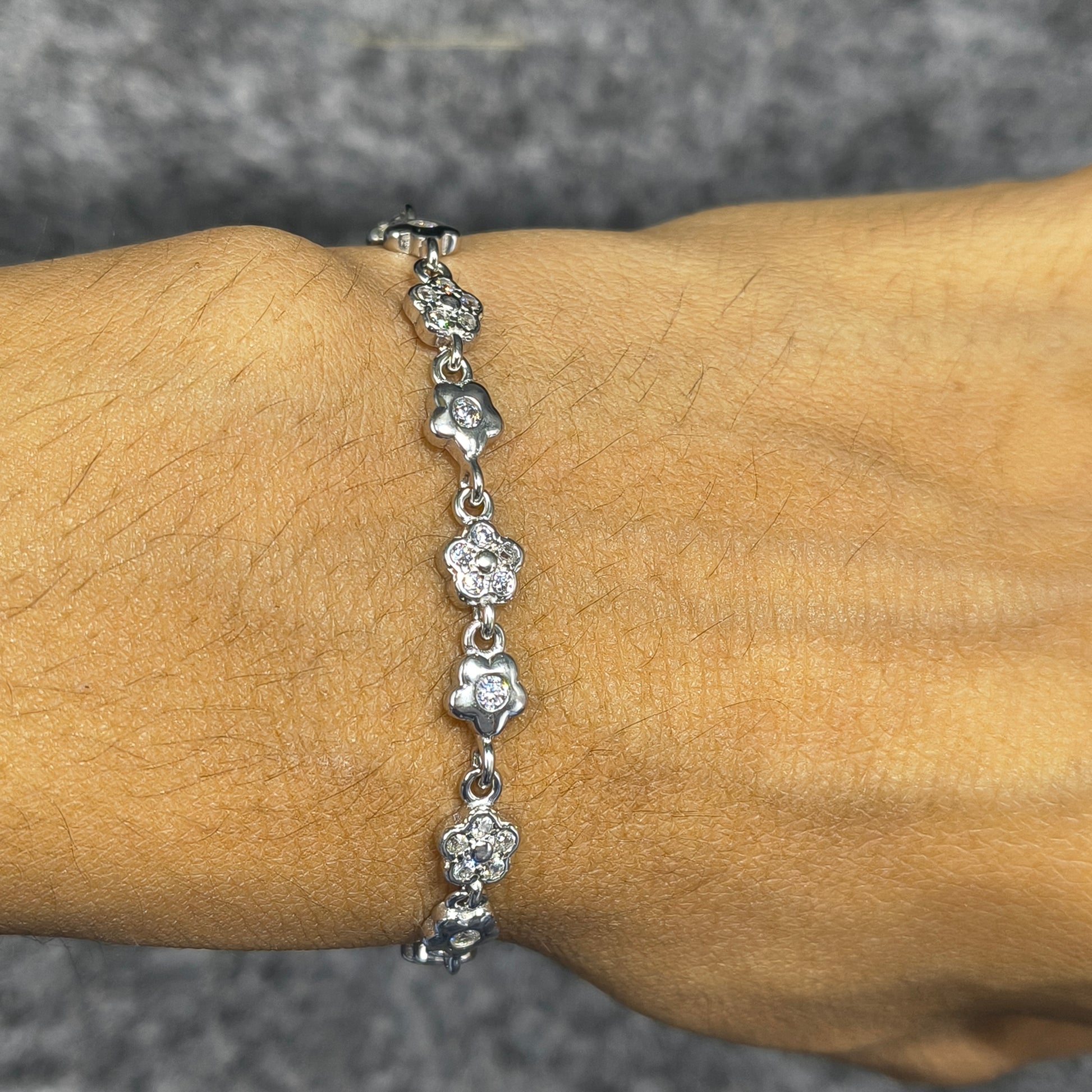 Silver bracelet with floral designs on a wrist against a neutral background