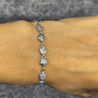 Silver bracelet with floral designs on a wrist against a neutral background
