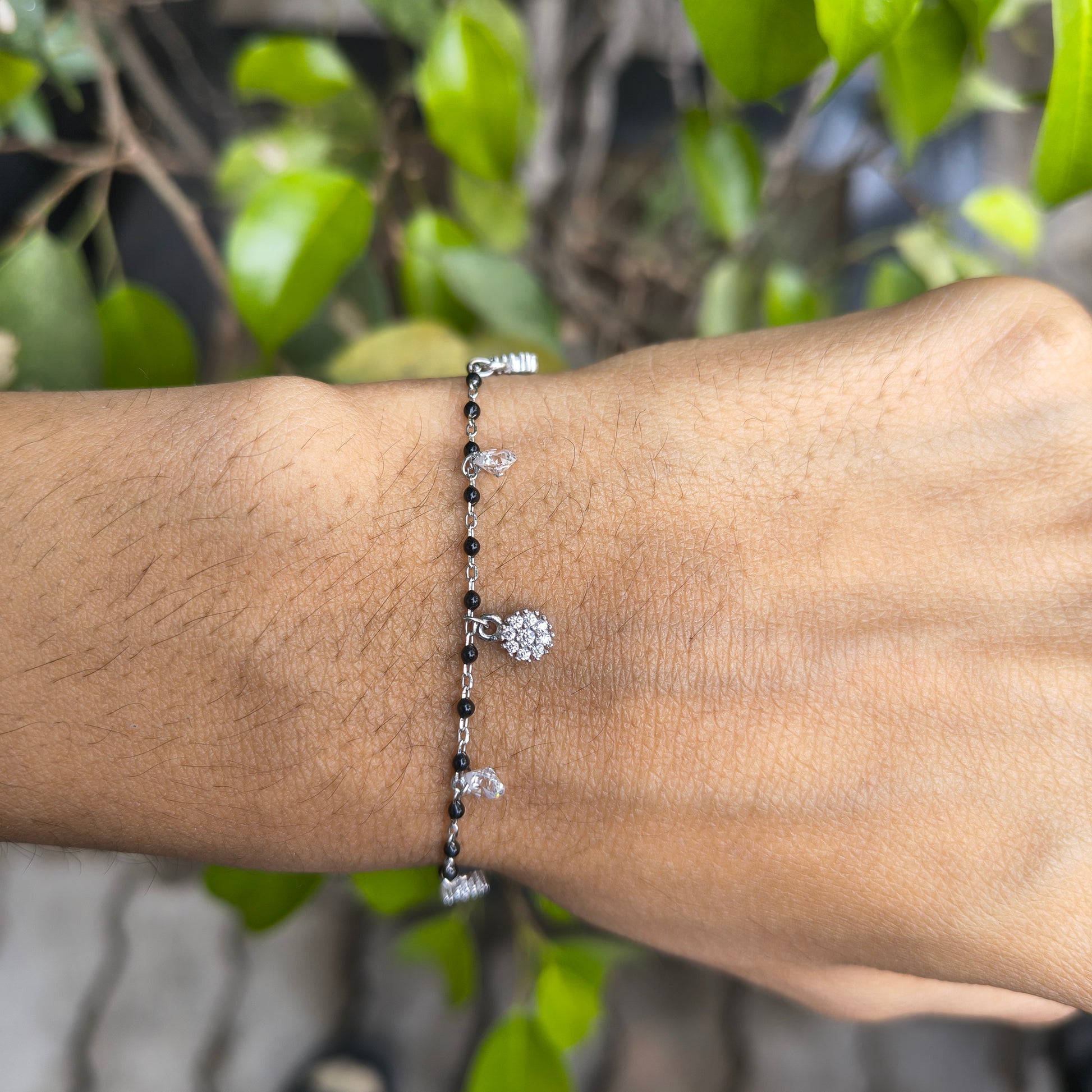 Bracelet with small tree charm on wrist against a natural background