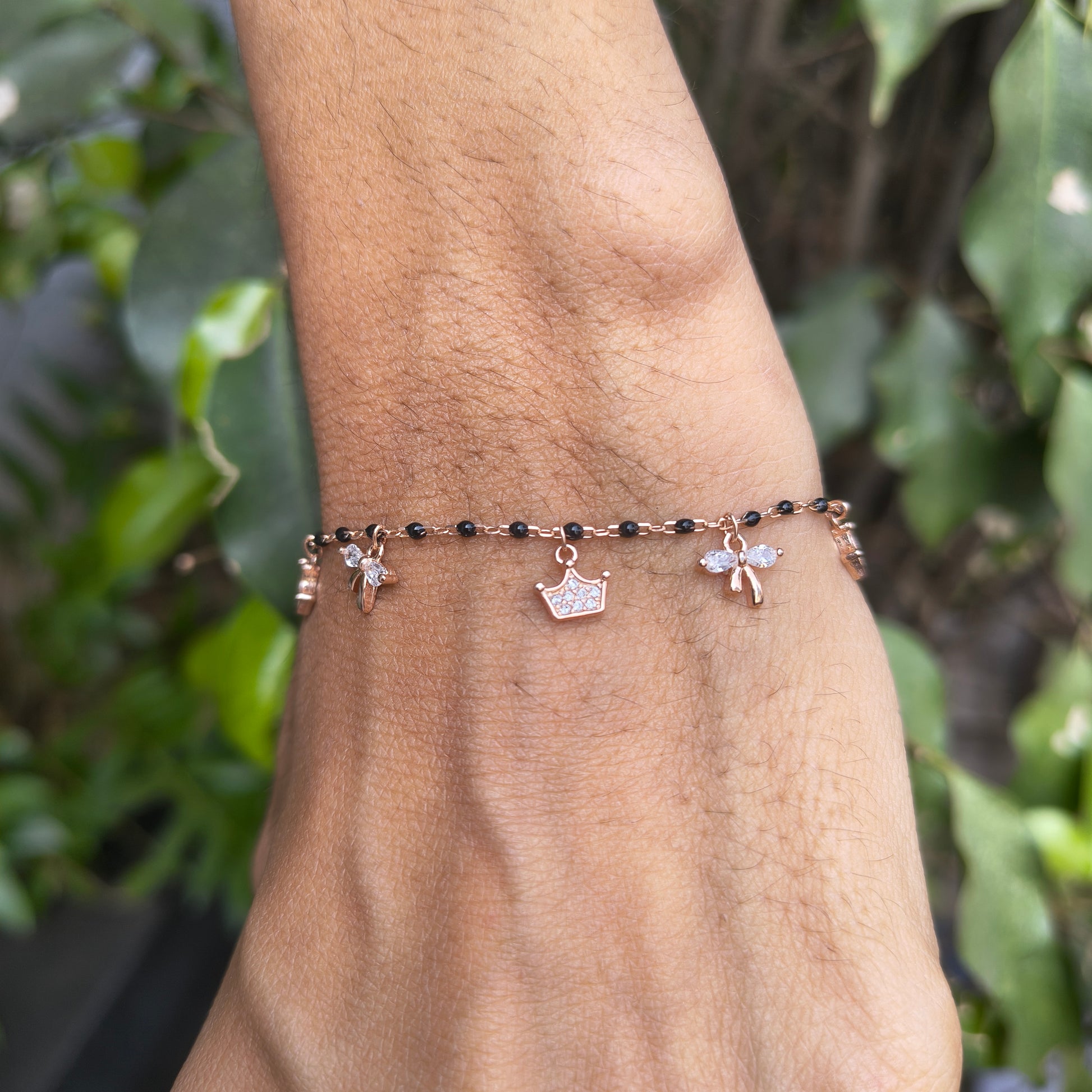 Bracelet with black beads and silver charms on a wrist against a green leafy background