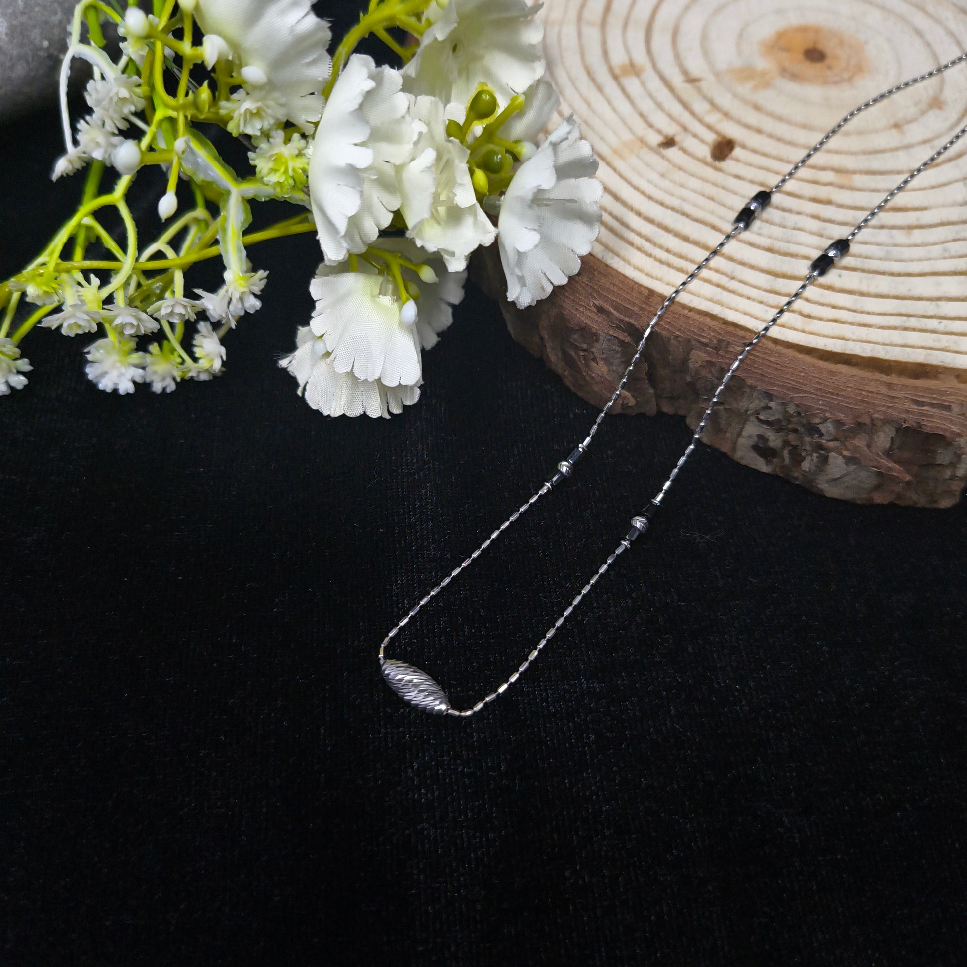 Necklace with black beads on a wooden block and white flowers against a dark background