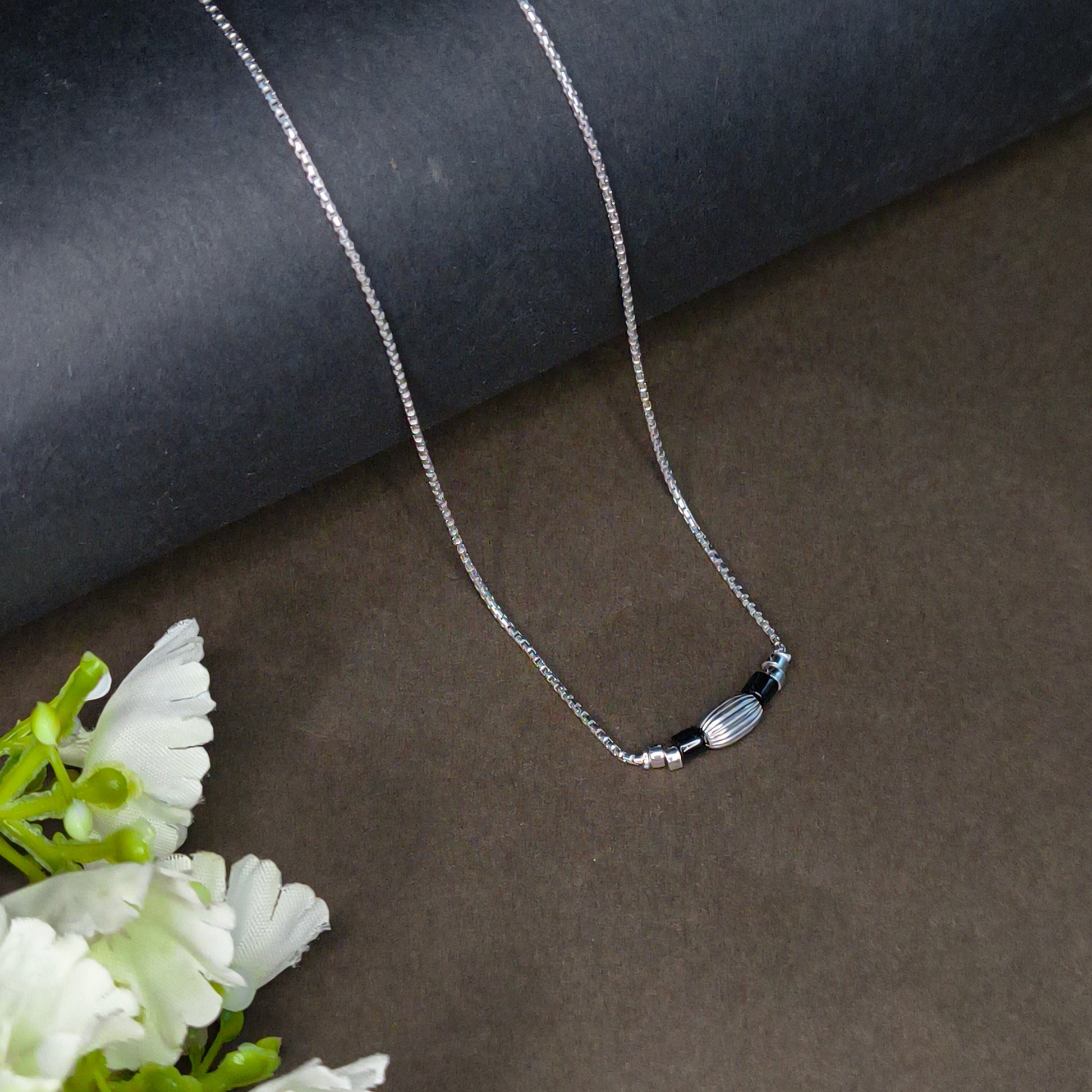 Silver necklace on a dark fabric background with white flowers