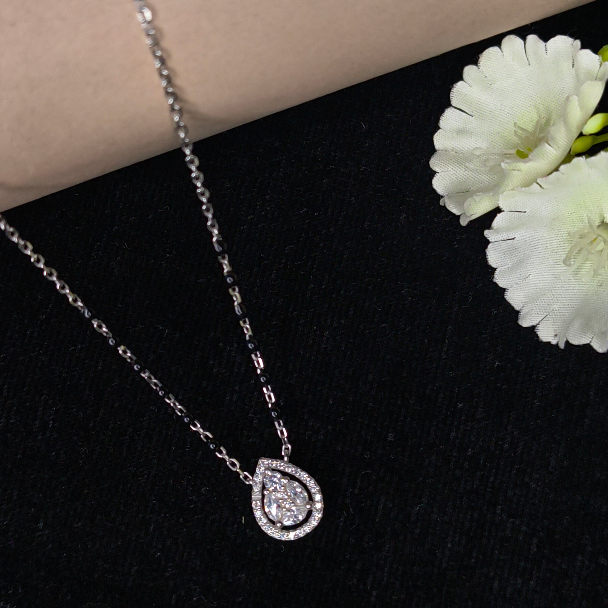 Silver chain necklace with a teardrop-shaped pendant on a black background with white flowers.