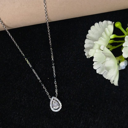 Silver necklace with a heart-shaped pendant on a black surface with white flowers.