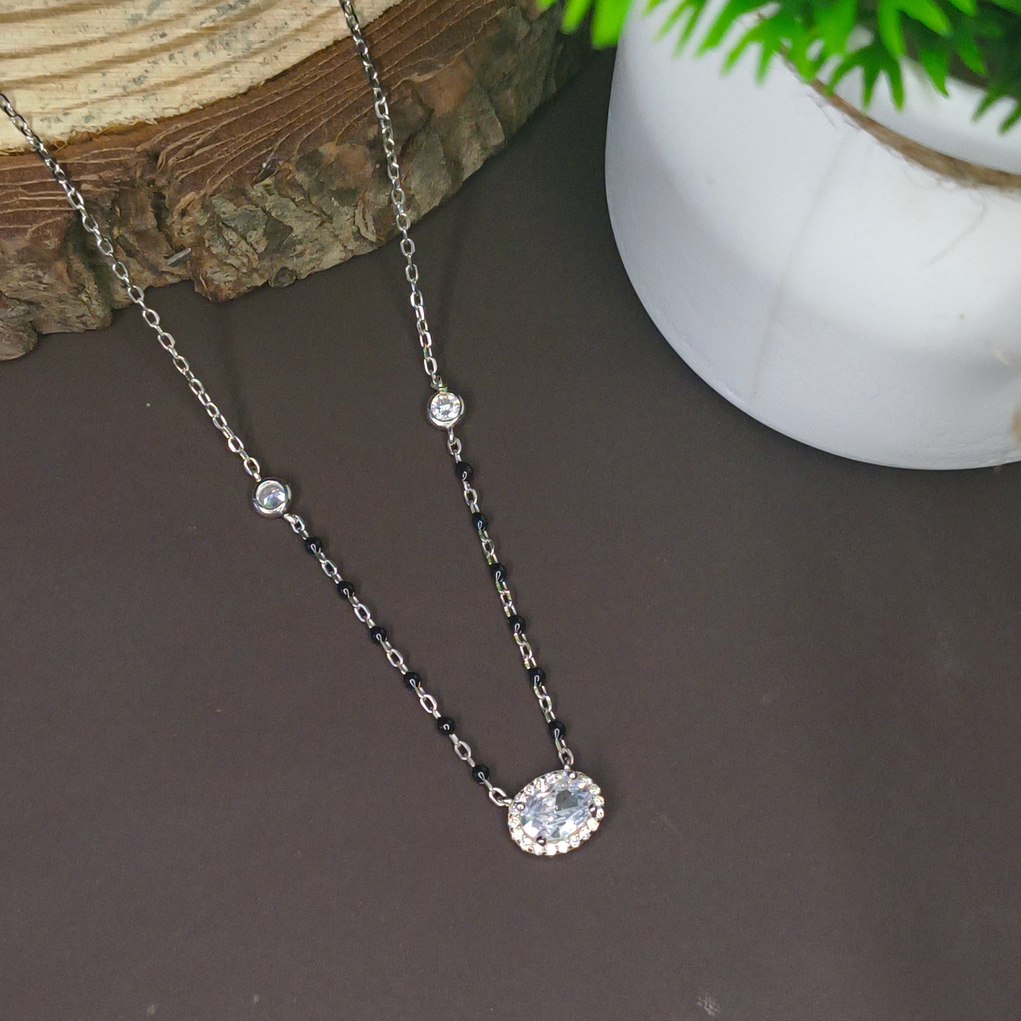Two necklaces on a dark surface with a plant in the background