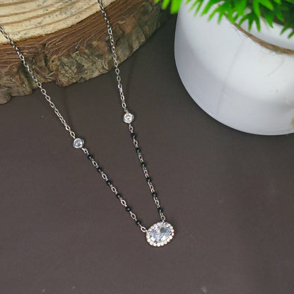 Two necklaces on a dark surface with a plant in the background