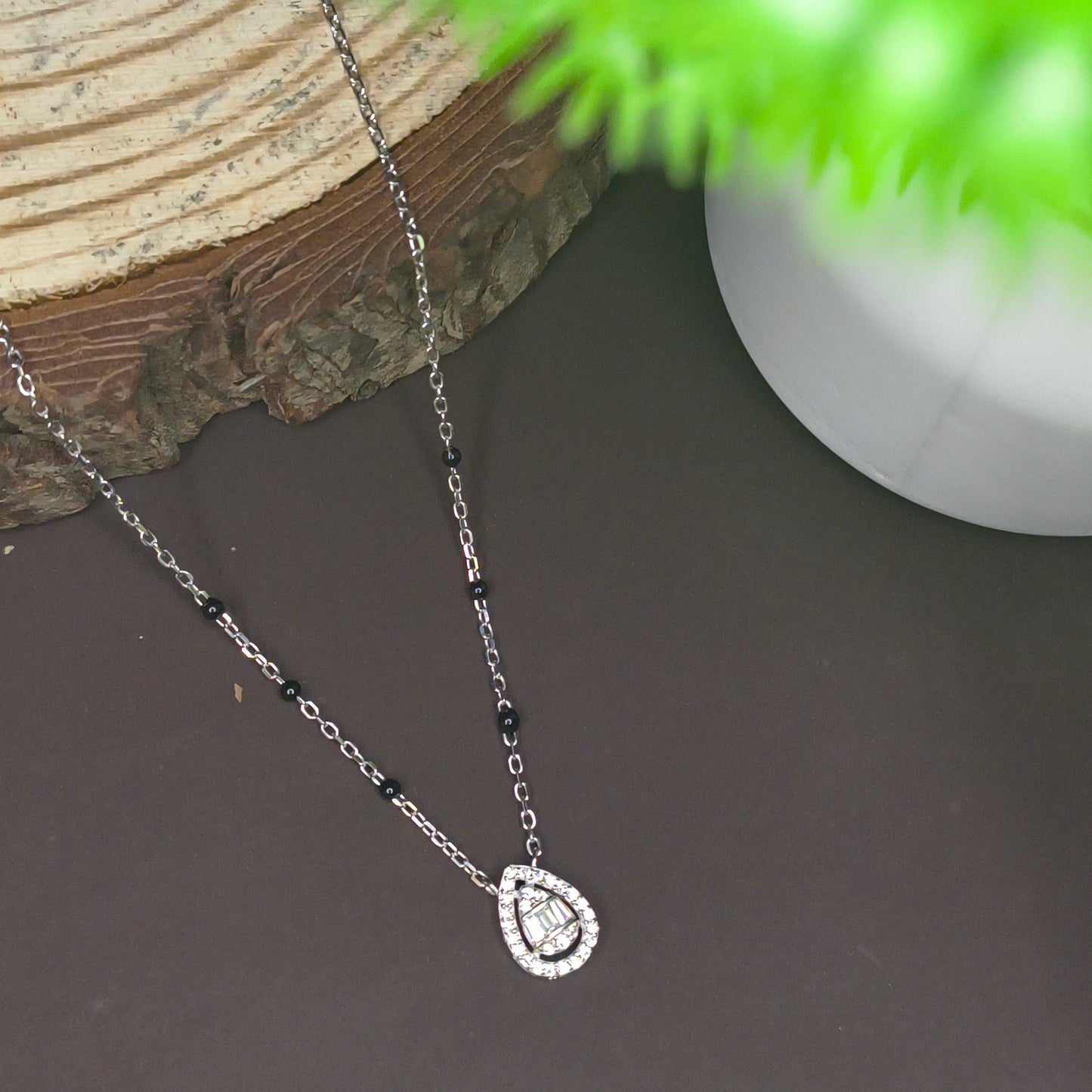 Necklace with a heart-shaped clasp on a dark surface with a plant in the corner