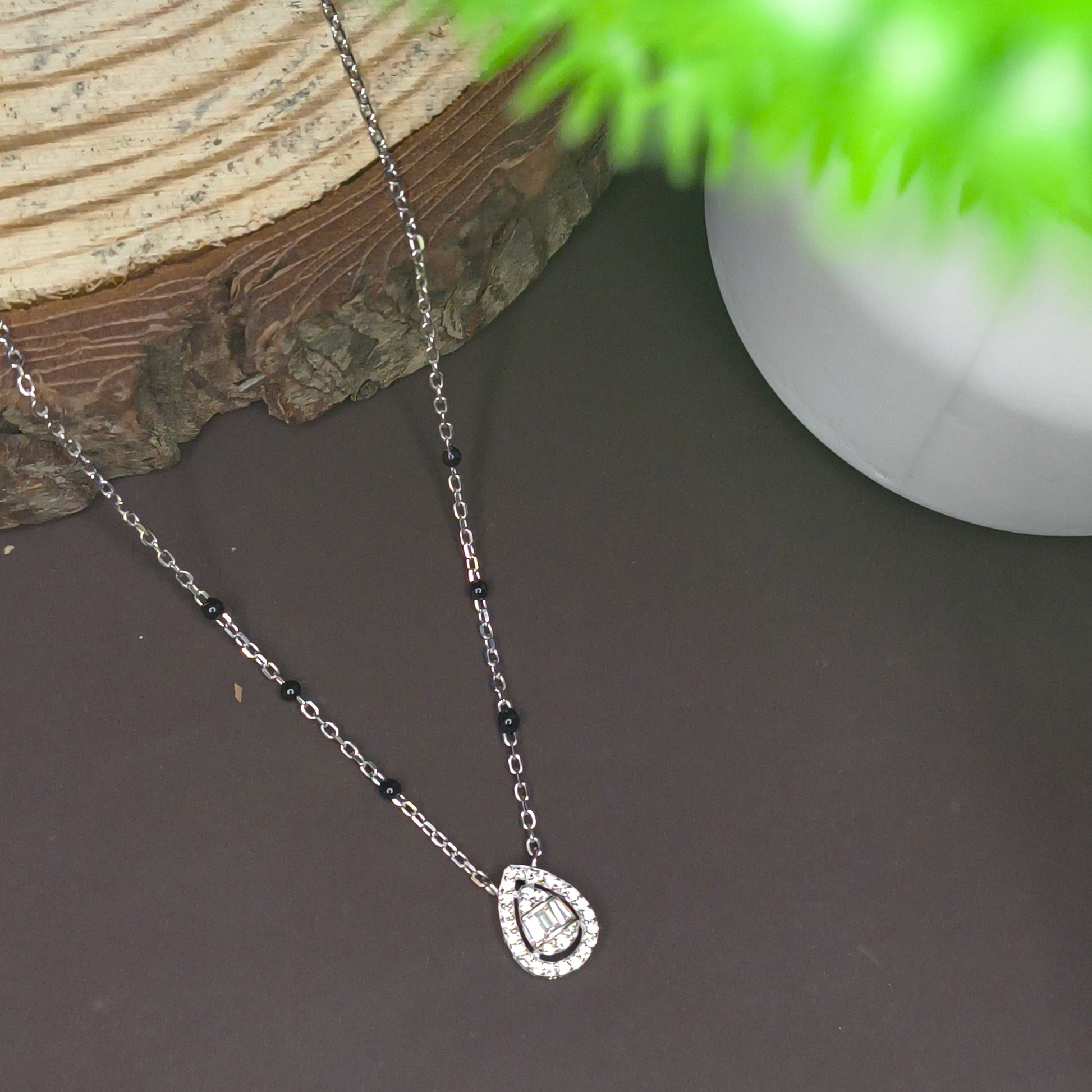 Necklace with a heart-shaped clasp on a dark surface with a plant in the corner
