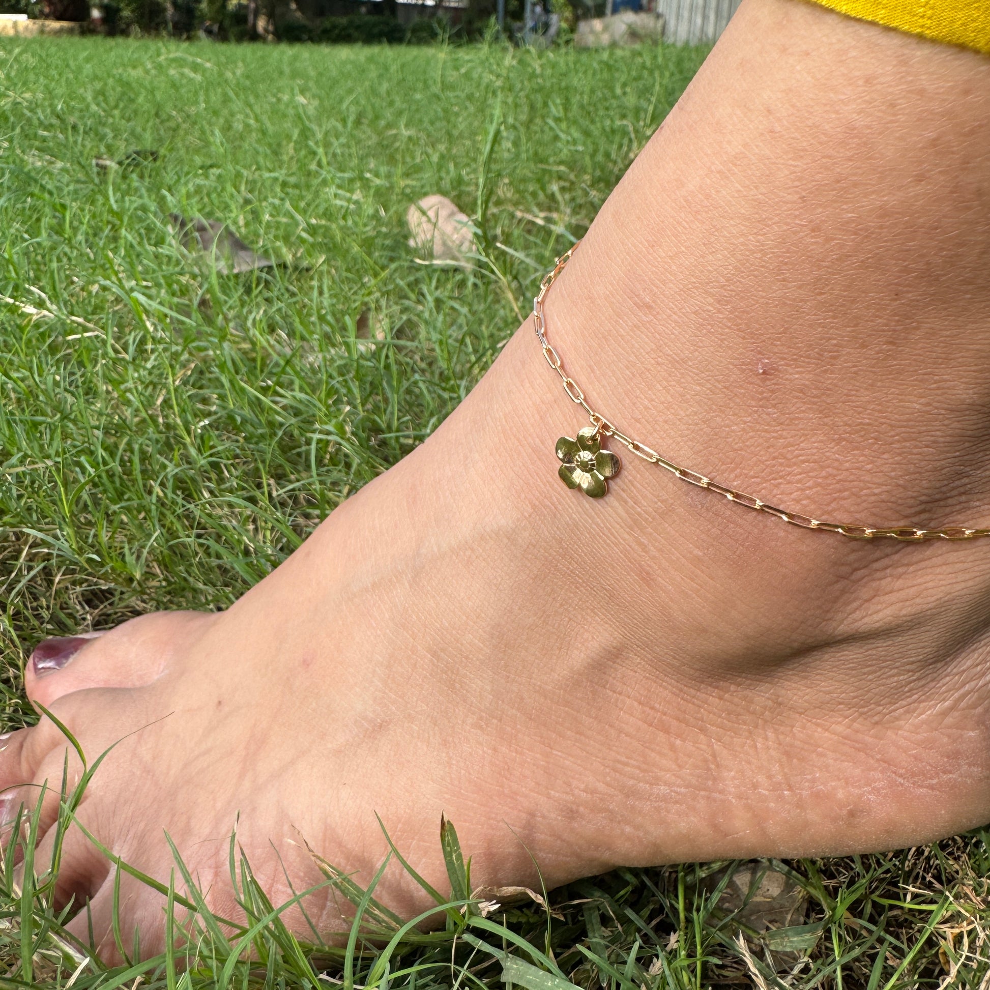 Gold anklet with a clover charm on a foot in grass