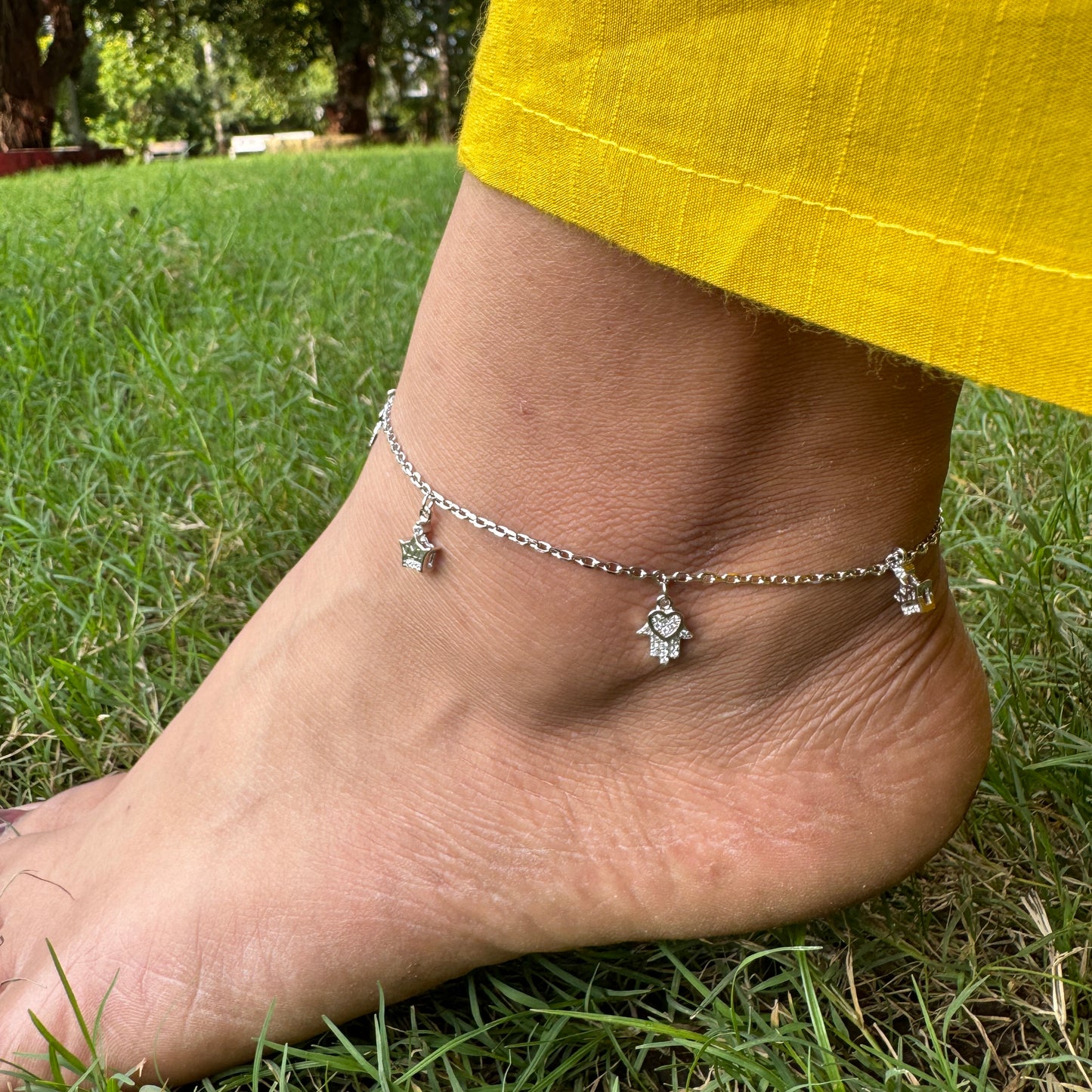 Ankle with silver anklet featuring charms on grass