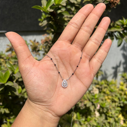 Hand holding a necklace with a pendant against a blurred green outdoor background