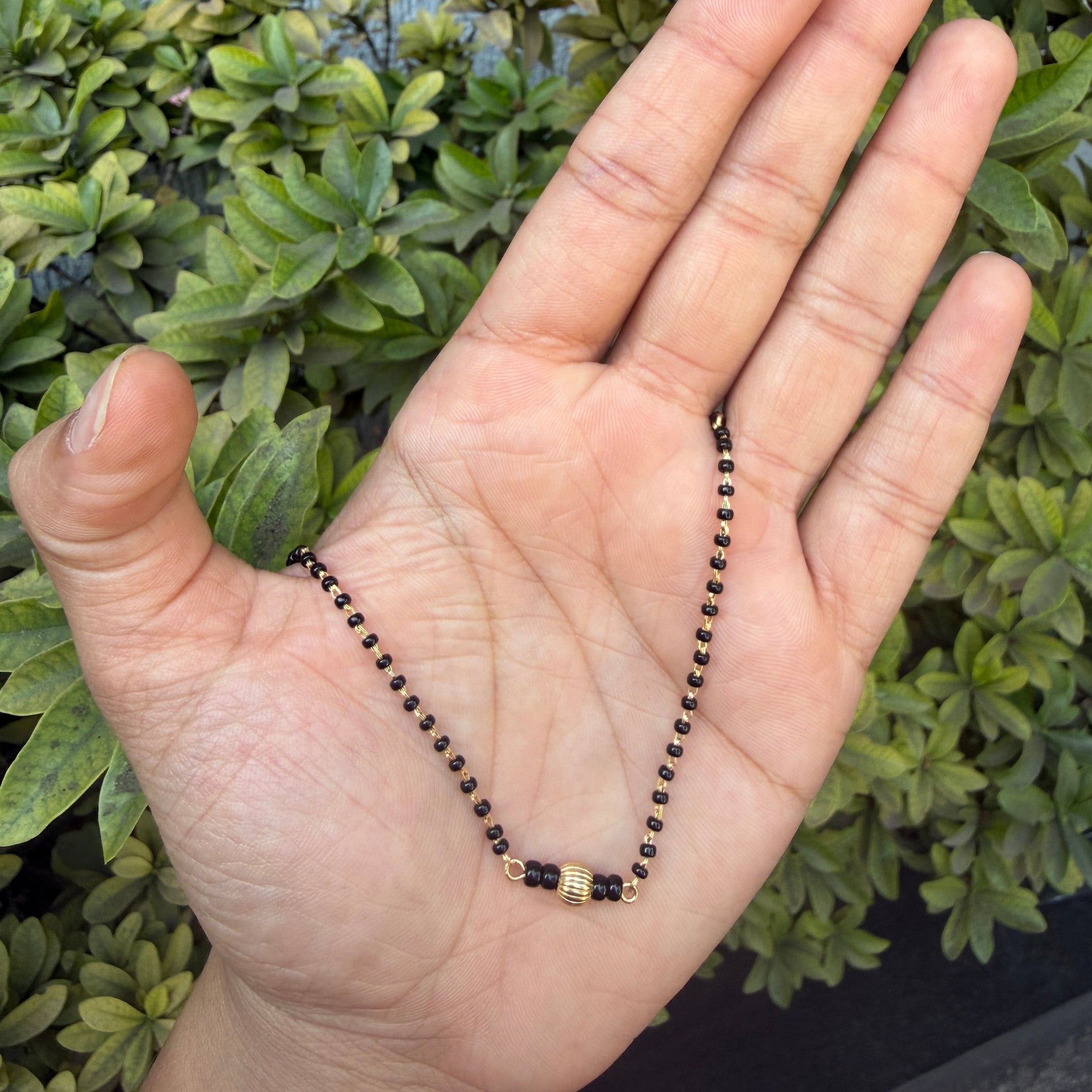 Hand holding a black and gold beaded necklace against a green leafy background