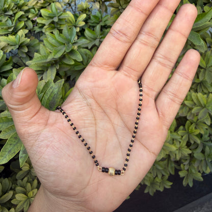 Hand holding a black and gold beaded necklace against a green leafy background