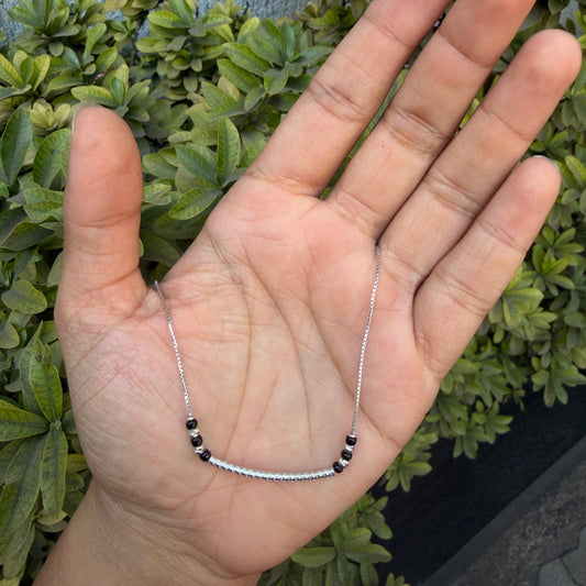 Hand holding a delicate silver bracelet with green foliage in the background