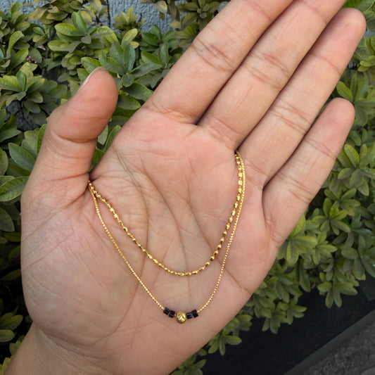 Gold necklace held in a hand with green foliage in the background