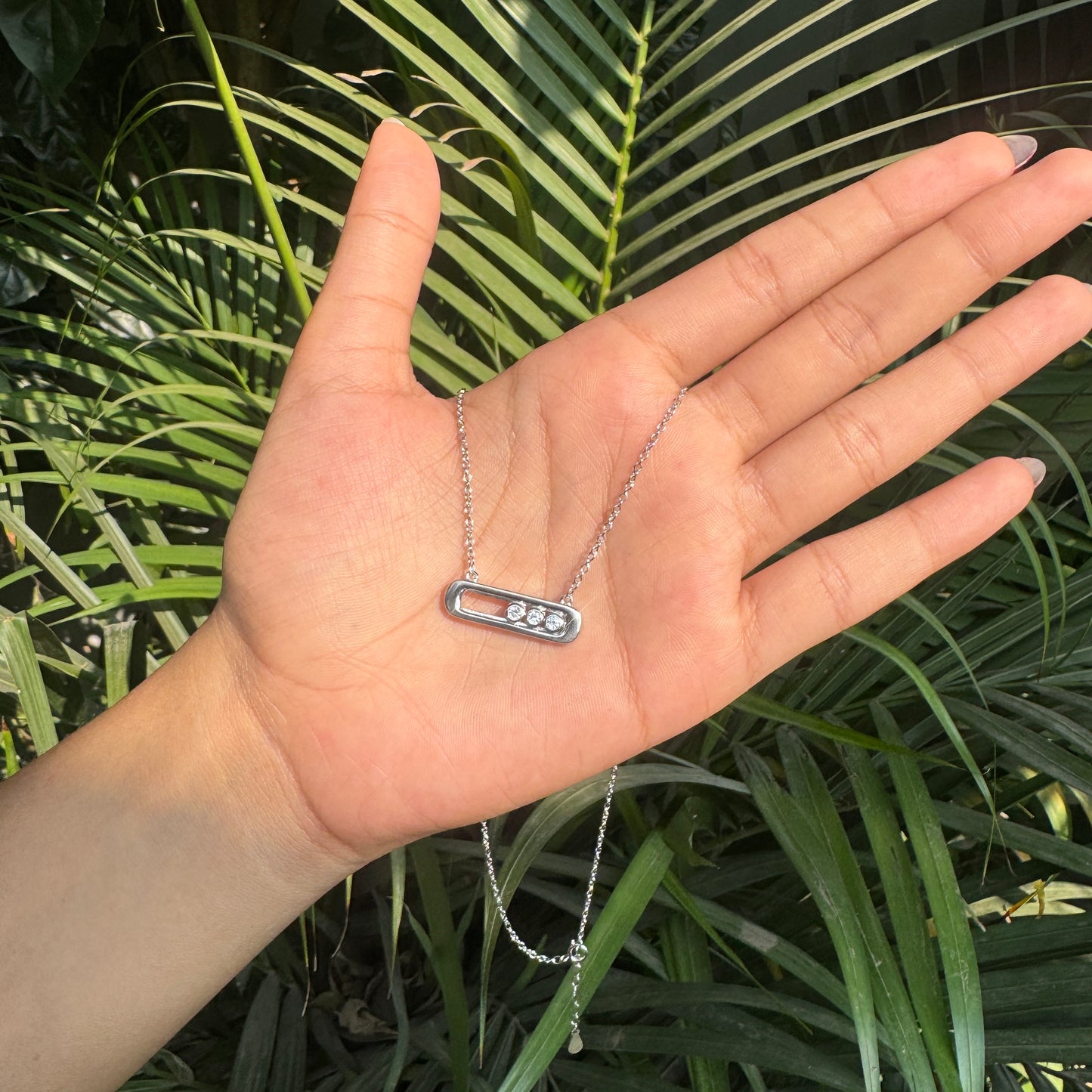 Hand holding a necklace with a green leafy background