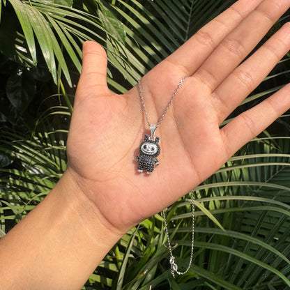 Hand holding a silver necklace with a detailed pendant against a green leafy background