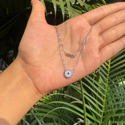 Hand holding a silver necklace with a blue gemstone pendant against a green leafy background
