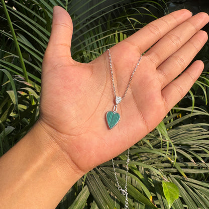 Hand holding a necklace with a heart-shaped pendant against a green leafy background