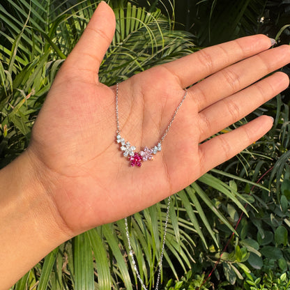 Hand holding a delicate necklace with floral design against a green leafy background